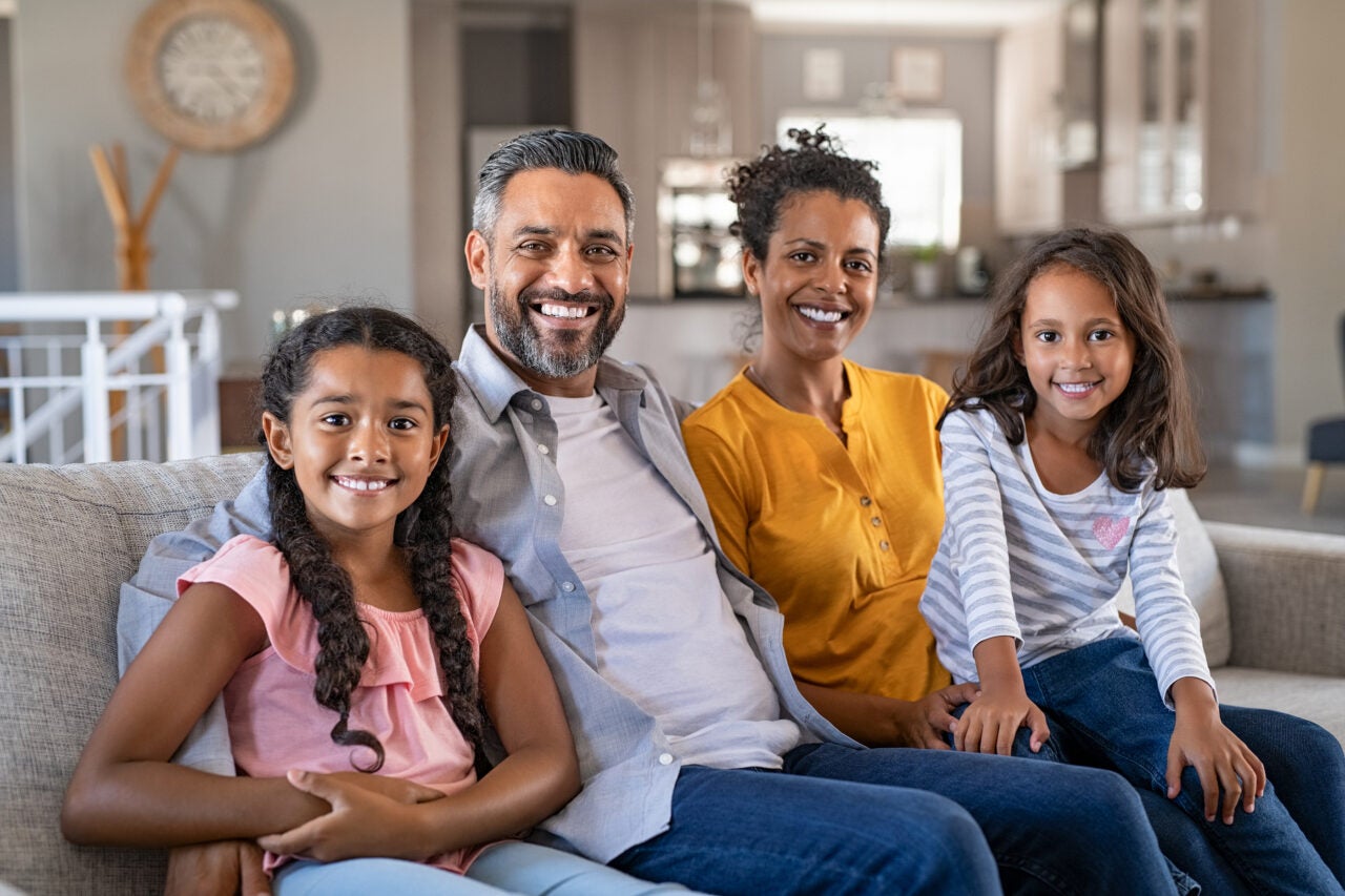 Portrait of cheerful ethnic family at home sitting on sofa.