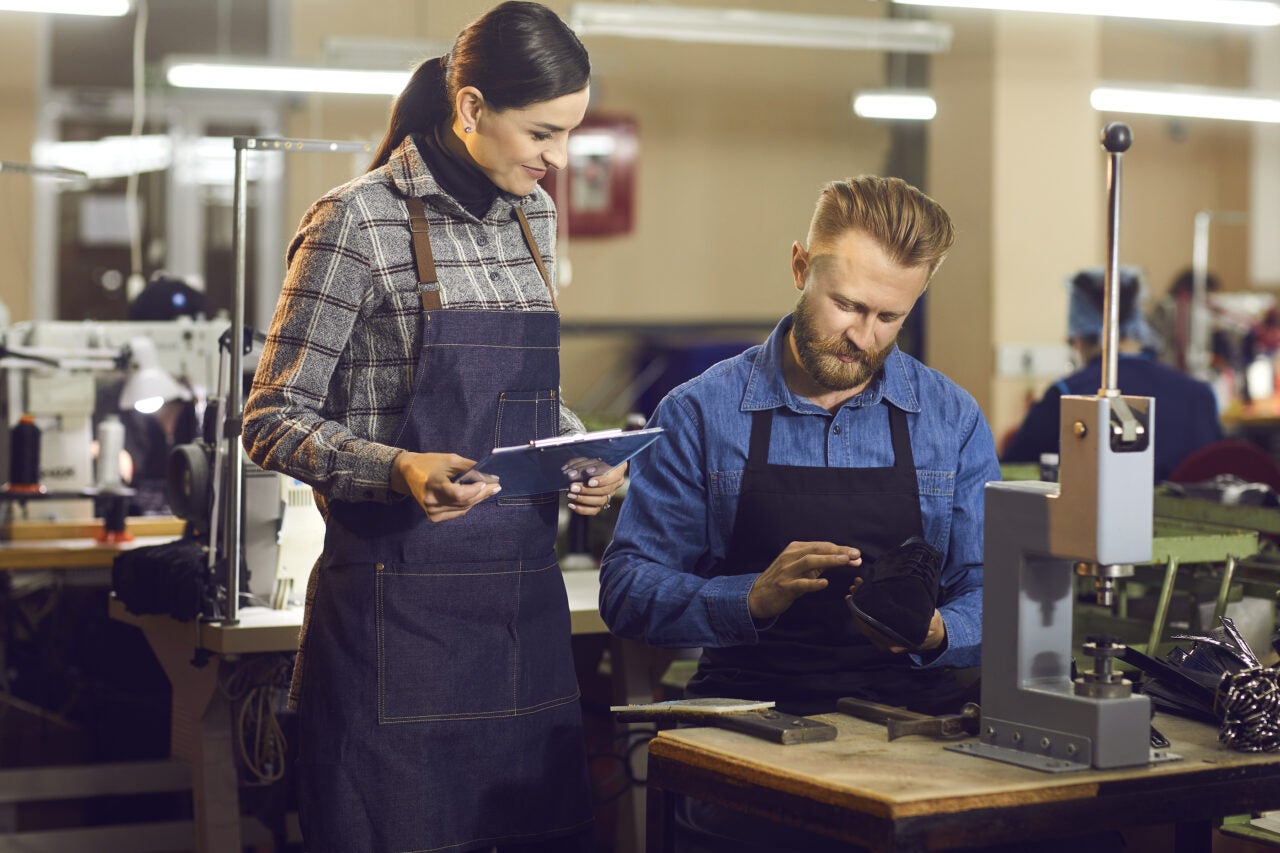 Two Shoe Factory Workers Checking The Quality Of New Footwear