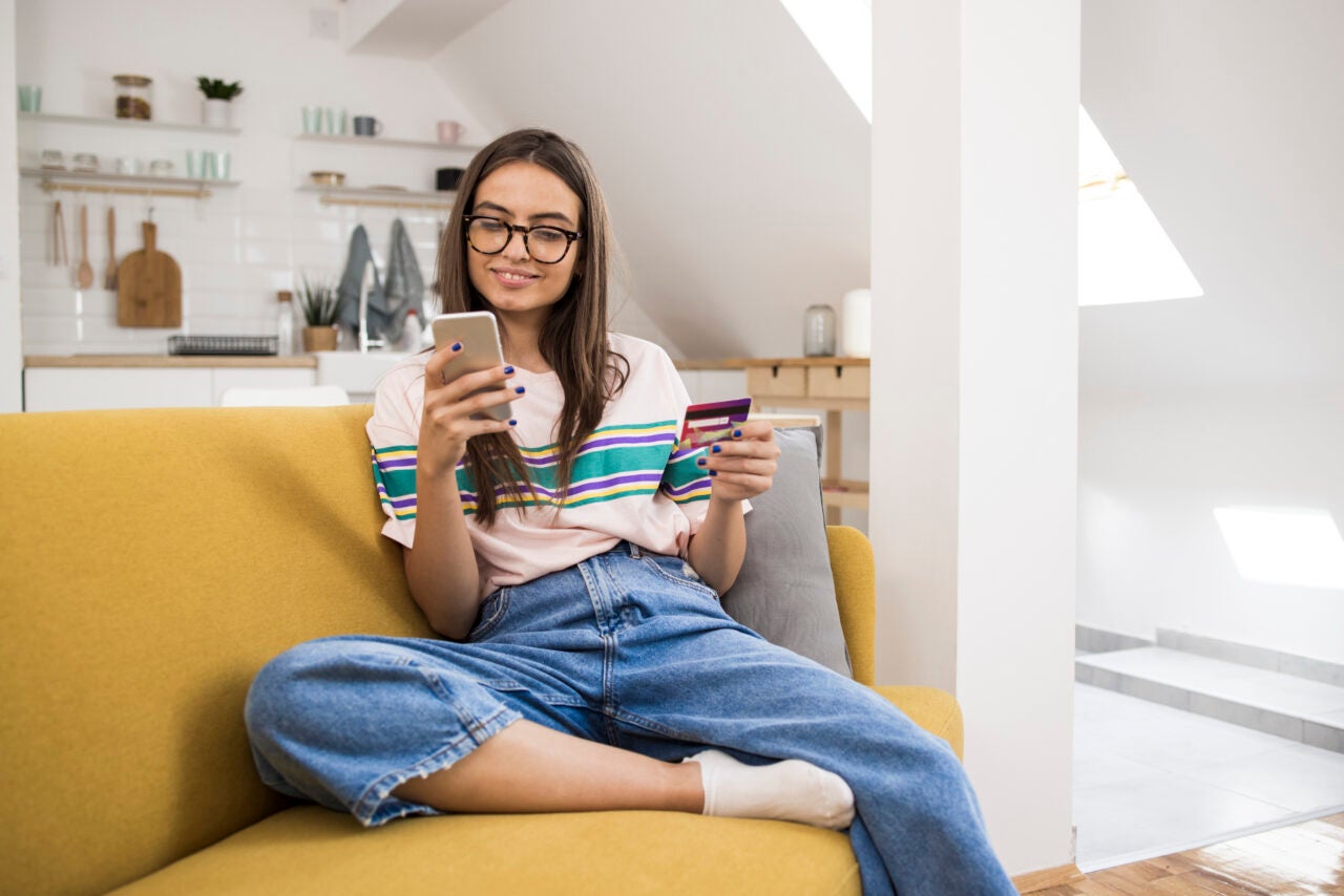 Young woman holding debit card and phone using her Access Personal Checking account from Coastal
